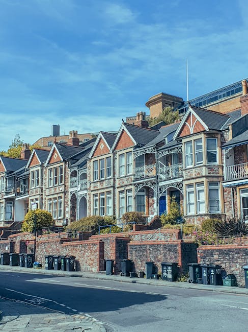 A street scene in Muswell Hill showing a row of multi-storey brick and stone residential buildings with bay windows and gabled roofs, situated along a busy road with several cars driving and parked al