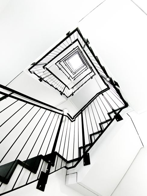 Inside a residential property showing a wooden staircase with dark handrails and decorative side panels, illuminated by natural light casting shadows on the steps. The staircase is part of a home undergoing a move, with no visible furniture or boxes on the stairs themselves. The surrounding walls are painted in a light colour, and the upward view highlights the elevation within the interior space. The scene suggests a focus on the staircase area during a home relocation process, with attention to the structural elements and lighting. Man with Van Muswell Hill’s removal services may involve managing furniture transport through this staircase, ensuring safe and efficient movement within the property.